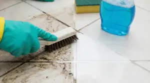 Mano con guanto pulisce fughe nere tra piastrelle con spazzola