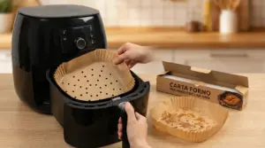 Mani che inseriscono un foglio di carta da forno forata nel cestello di una friggitrice ad aria su un piano cucina